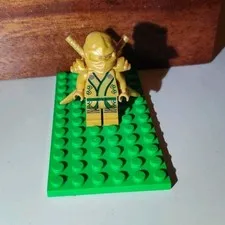 LEGO Gold Ninja Minifigure with Swords/Accessories on Green Baseplate